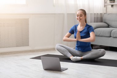 Huzurlu kadın laptopun yanında online yoga meditasyonu yapıyor.