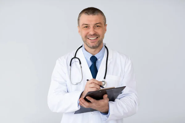 Portrait of mature doctor writing something on clipboard — Stock Photo, Image