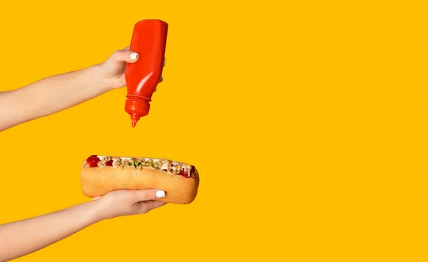 Aproape de o femeie tânără stoarce ketchup pe hot dog pe fundal portocaliu, copia spațiu. Panorama — Fotografie, imagine de stoc