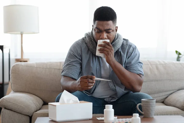 Příznaky koronaviru. Nemocný africký muž kontroluje tělesnou teplotu doma — Stock fotografie