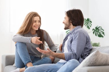 Neşeli çift sohbet ediyor, evdeki koltukta oturuyor.