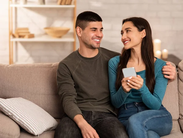 Casal usando telefone celular sentado no sofá, espaço livre — Fotografia de Stock