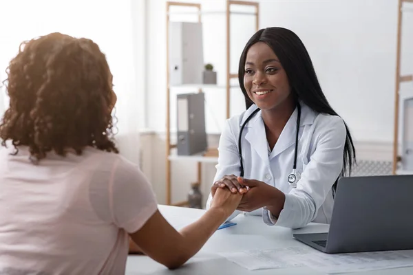 Cheerful female doctor holding patient hand, clinic interior