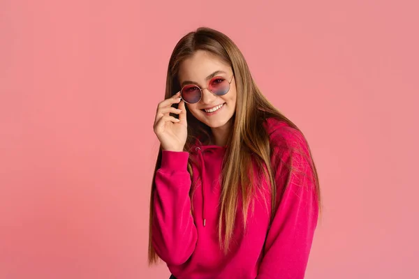 Sonriente chica pone su mano a las gafas de color rosa — Foto de Stock