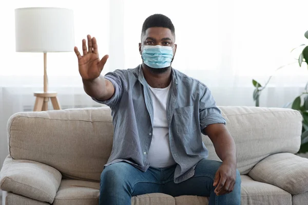 Magabiztos afrikai férfi visel orvosi maszkot otthon, és bemutatja Stop Gesture — Stock Fotó
