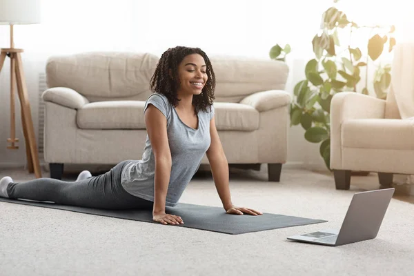 Black Girl Practicing Yoga Στο σπίτι με φορητό υπολογιστή, βλέποντας σε απευθείας σύνδεση μαθήματα — Φωτογραφία Αρχείου