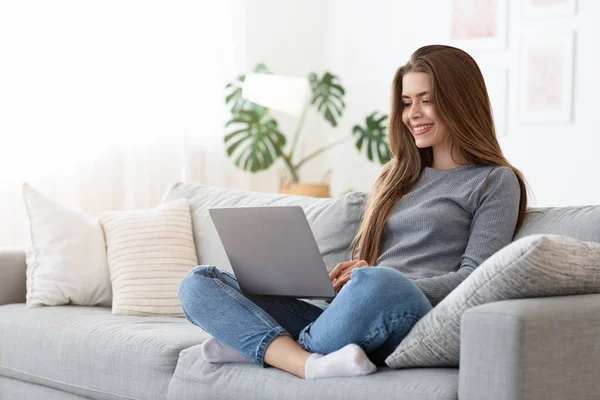 Mujer joven feliz usando el ordenador portátil en el sofá en casa —  Fotos de Stock