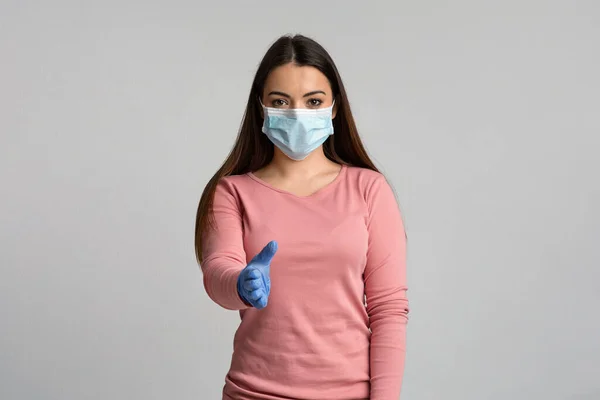 Jonge vrouw in medische masker en handschoenen uit te breiden hand voor handdruk — Stockfoto