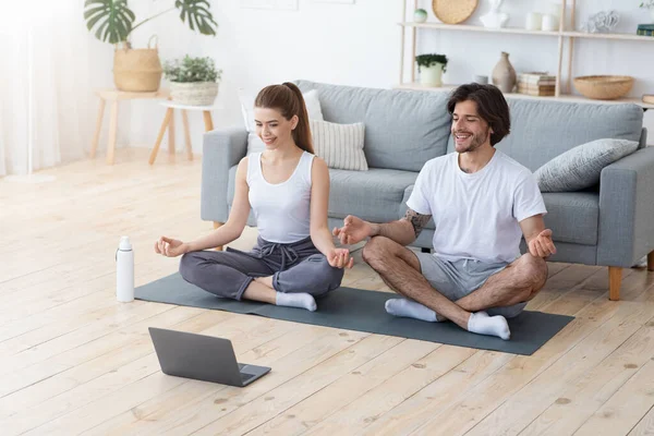 Sportliches Paar meditiert zu Hause, schaut auf Laptop-Bildschirm — Stockfoto