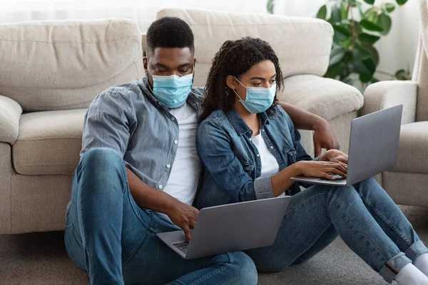 Fiatal fekete pár visel orvosi maszkok dolgozik a laptopok otthon — Stock Fotó