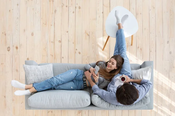 Jovem casal pacífica usando gadgets enquanto descansa em casa — Fotografia de Stock