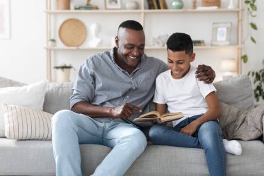 Olgun Afro-Amerikan bir adam torunuyla birlikte kitap okuyor.