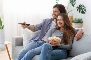 Mutlu çift evde film izliyor, patlamış mısır yiyor.