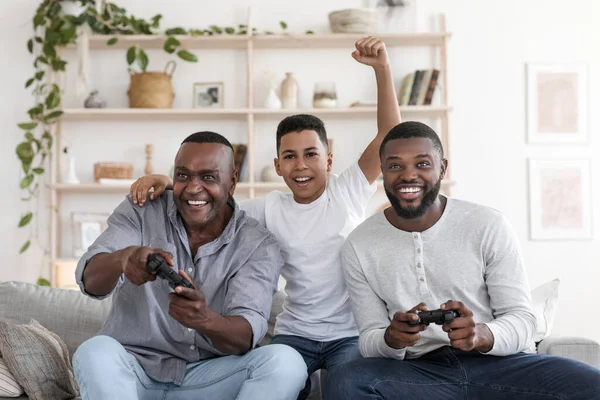 Allegro ragazzo nero che gioca ai videogiochi con padre e nonno a casa — Foto Stock