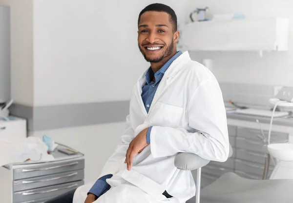 Homem negro alegre estomatologista descansando no local de trabalho — Fotografia de Stock