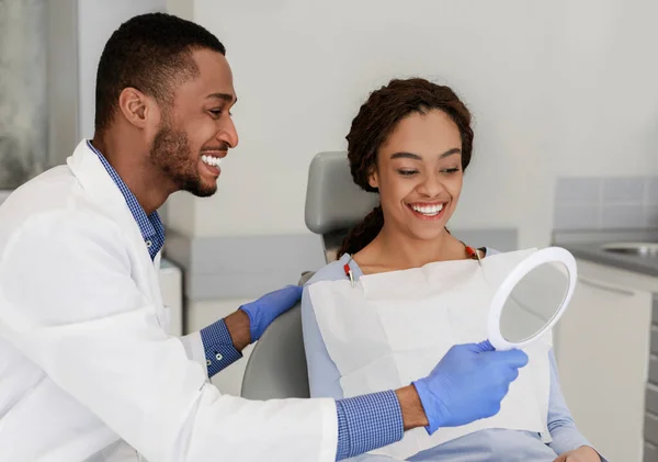 Φιλικός μαύρος οδοντίατρος δίνει καθρέφτη στον χαρούμενο ασθενή του — Φωτογραφία Αρχείου