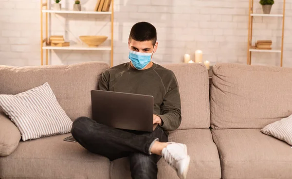 Man wearing surgical mask using his laptop — Stock Photo, Image