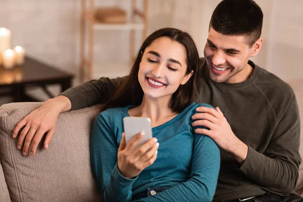 Пара с помощью мобильного телефона сидит на диване — стоковое фото