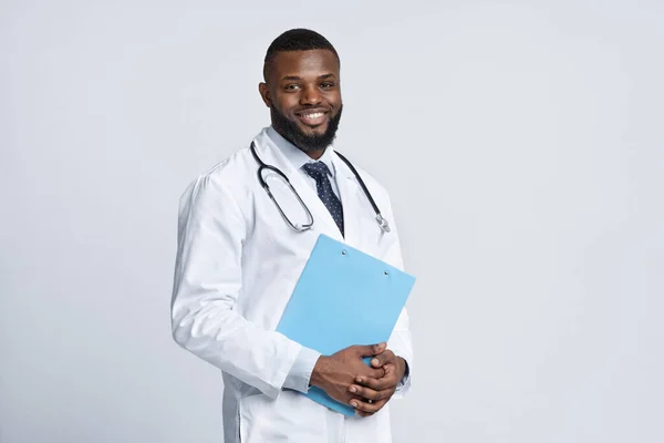 Veselý černý terapeut drží lékařskou kartu nad bílou — Stock fotografie