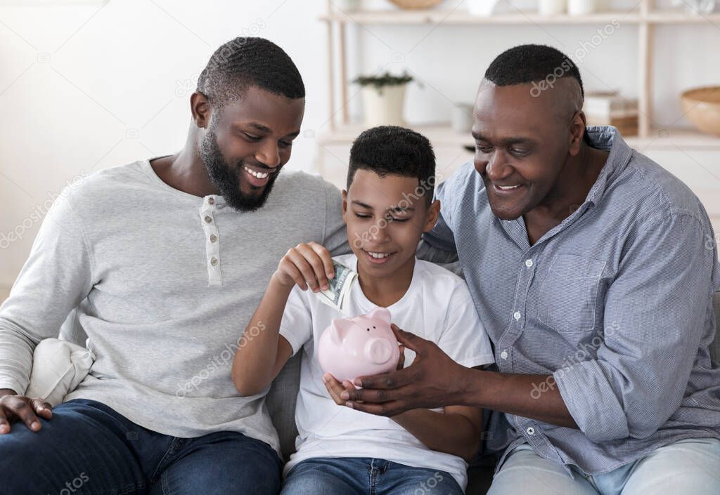 Black Preteen Boy With Father And Grandfather Putting Money To Piggybank
