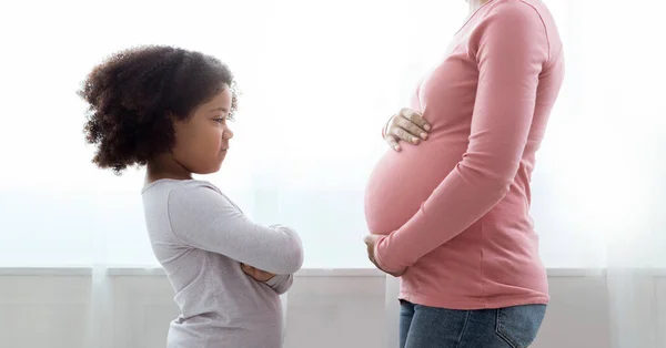 Malá černošky dívka při pohledu na její těhotné maminky břicho s žárlivostí — Stock fotografie