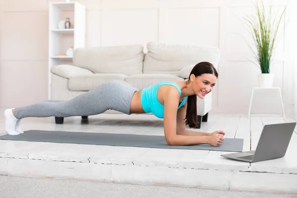 Fit meisje training op laptop doen Plank oefening thuis — Stockfoto