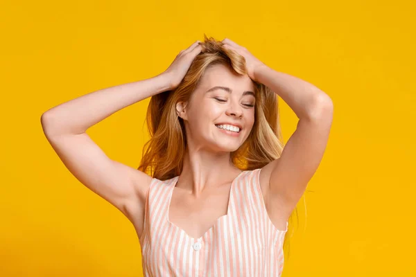 Sólo feliz. Jovencita alegre tocando su cabello de pie sobre fondo amarillo —  Fotos de Stock