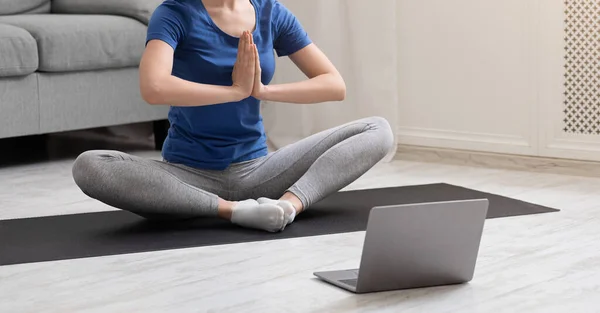 Sporty girl meditating in lotus position near laptop at home