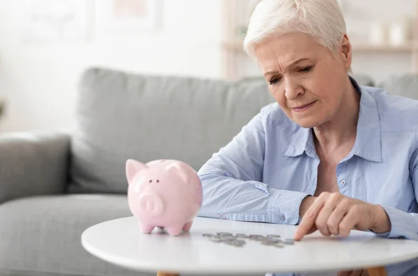 Sem poupanças. Mulher idosa perturbada contando moedas do banco porquinho — Fotografia de Stock
