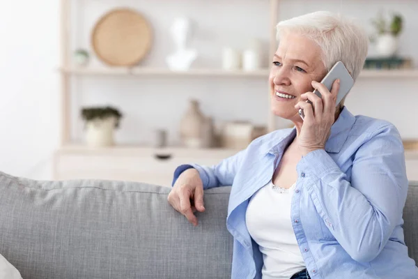 Современная коммуникация. Улыбающаяся пожилая женщина разговаривает по телефону дома — стоковое фото