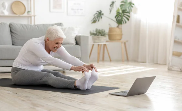 Mulher sênior ativa fazendo exercícios de alongamento de aquecimento na frente do laptop — Fotografia de Stock