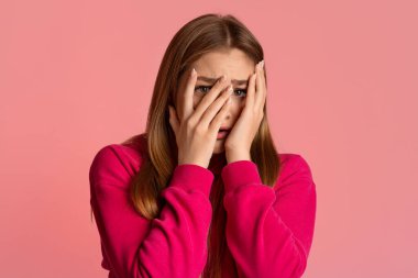 Kız elleriyle yüzünü kapatıyor ve parmaklarının arasından bakıyor.