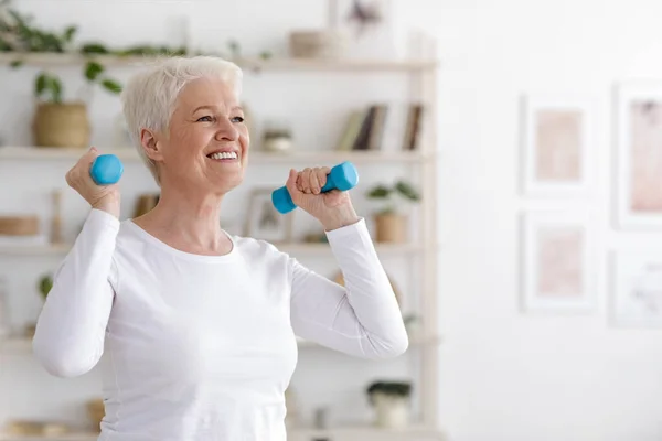 Estilo de vida saudável. Sorrindo Senior Lady Exercício com halteres em casa — Fotografia de Stock