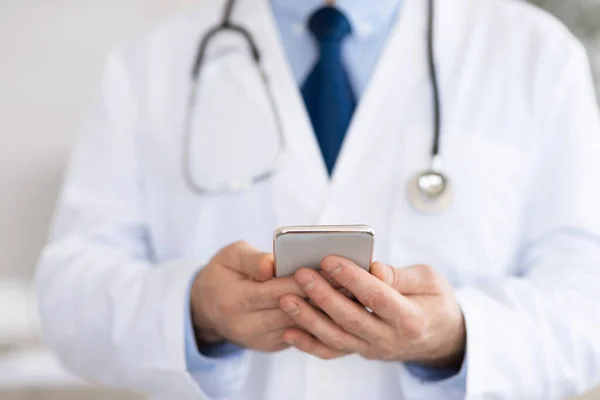 Medico utilizzando smartphone sul posto di lavoro, messaggistica con i pazienti — Foto Stock