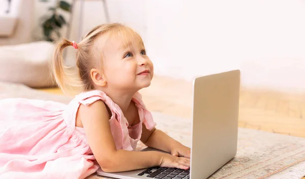 Imádnivaló kislány laptoppal fekszik a padlón. — Stock Fotó