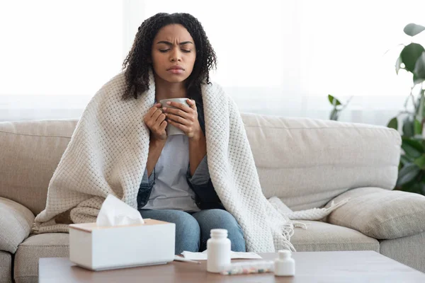Doente mulher negra sentindo-se mal em casa, bebendo chá no sofá — Fotografia de Stock