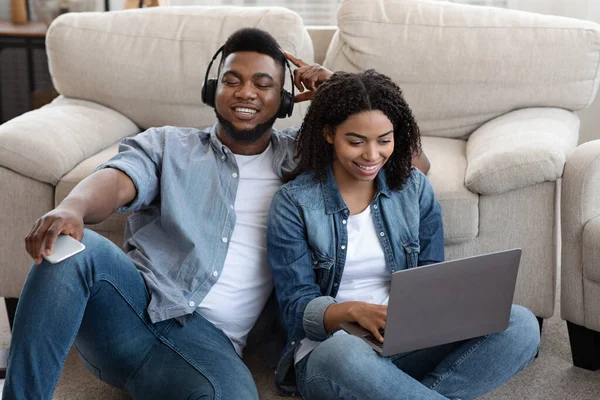 Μαύρο ζευγάρι χαλαρώνοντας μαζί στο σπίτι, ακούγοντας μουσική και χρησιμοποιώντας φορητό υπολογιστή — Φωτογραφία Αρχείου