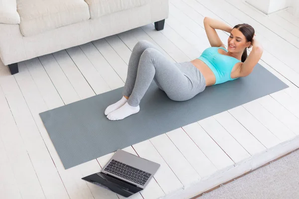 Sportliche Frau beim Abs-Training am Laptop zu Hause — Stockfoto