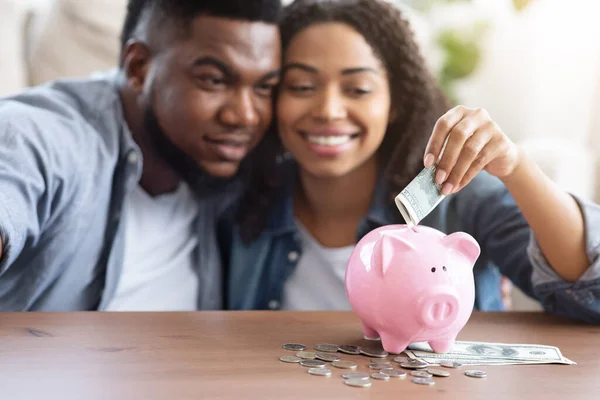 Orçamento Familiar. feliz casal preto colocando dinheiro para Piggybank em casa — Fotografia de Stock