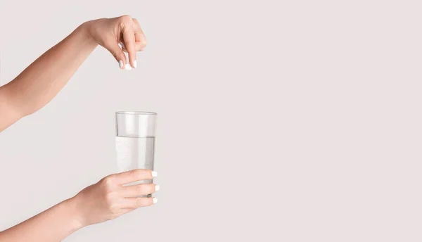 Weibliche Hände, die Tabletten in ein Glas Wasser auf hellem Hintergrund fallen lassen, Nahaufnahme. Leere Räume. Panorama — Stockfoto
