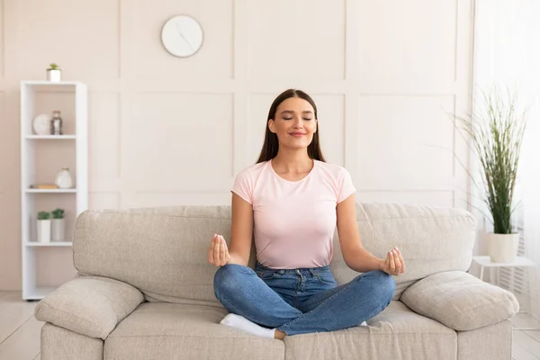 Спокойная девушка медитирует сидя в позе лотоса на диване — стоковое фото