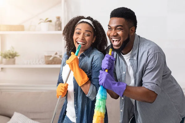 Εργασίες στο σπίτι με διασκέδαση. Αφρικάνικο ζευγάρι καθαρίζει το σπίτι μαζί, τραγουδά και κοροϊδεύει — Φωτογραφία Αρχείου