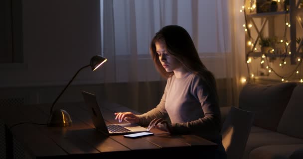 Chica joven freelancer escribiendo en el ordenador portátil en casa, trabajando hasta tarde — Vídeos de Stock