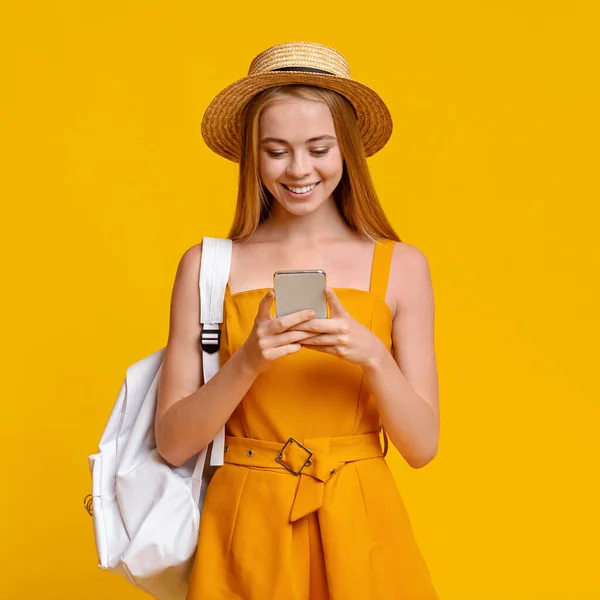 Concepto de Sim de viaje. Turista chica con mochila usando Smartphone sobre fondo amarillo — Foto de Stock