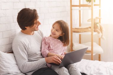 Baba ve kızı yatak odasında dizüstü bilgisayar kullanıyorlar.