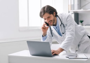 Doktor hastaya cep telefonuyla danışmanlık yapıyor ve dizüstü bilgisayarla çalışıyor.