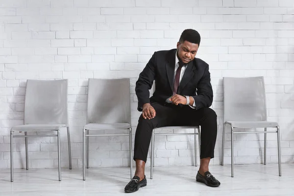 Millennial afro-americano à espera de entrevista de emprego, olhando para o seu relógio no lobby do escritório. Espaço vazio. — Fotografia de Stock