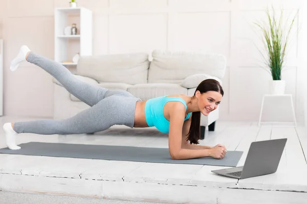 Sportowa dziewczyna ćwiczy na laptopie stojąc na desce w domu — Zdjęcie stockowe