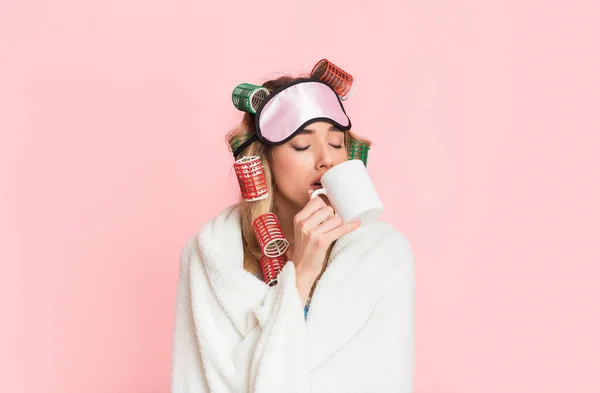 Donna assonnata in bigodini e maschera del sonno avvolto in coperta e beve caffè dalla tazza — Foto Stock