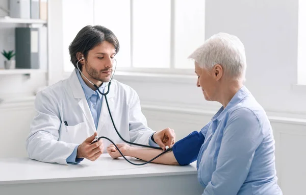 Médico joven midiendo la presión arterial de la mujer mayor — Foto de Stock
